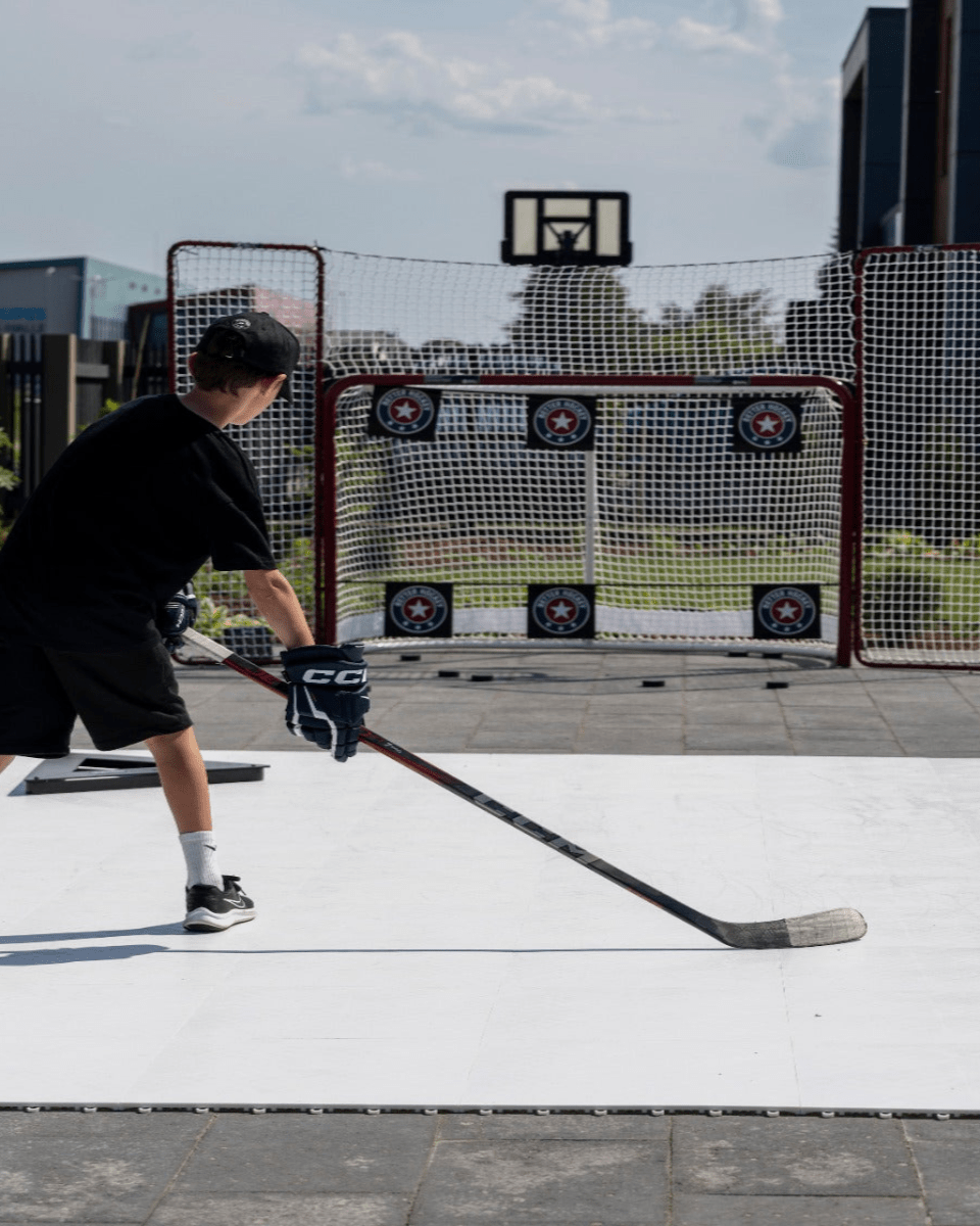 Ung kille övar hockeyskott på ett plastis hockeygolv med mål bakom sig, perfekt för torrlandsträning.