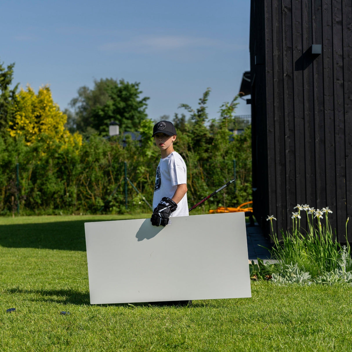 Ett barn bär en skottplatta hockey 120x60 cm på en grön gräsmatta, redo att träna sina hockeyfärdigheter hemma.