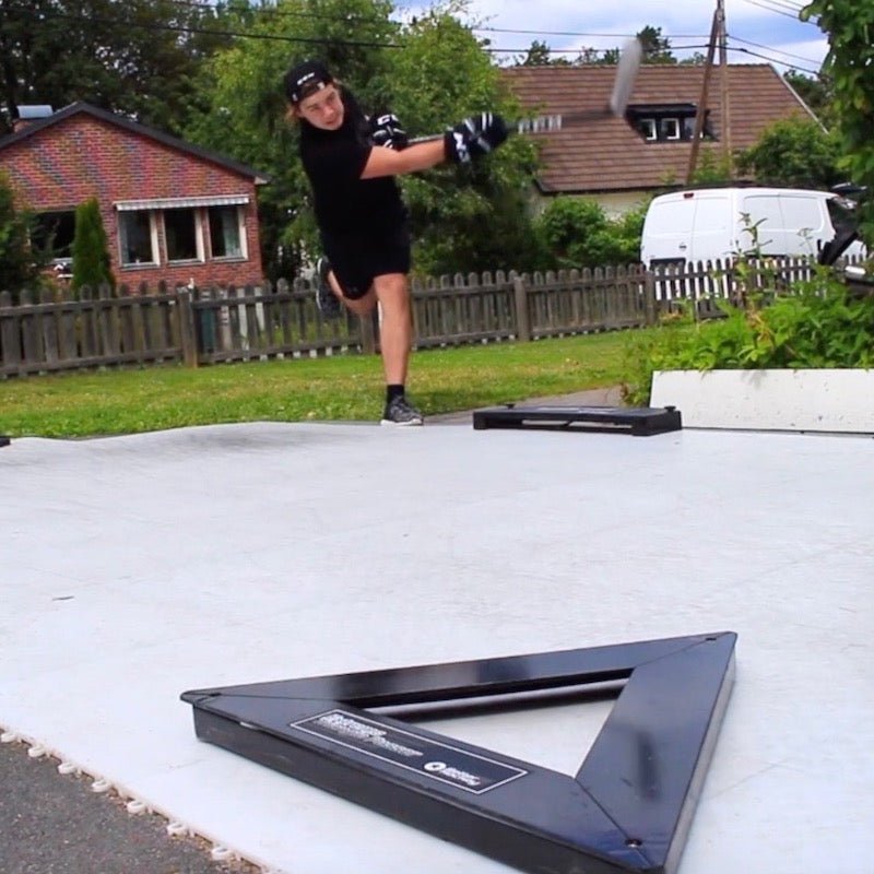 En spelare som använder Extreme Hockey Flooring Tiles på gräsmatta och slår puck med en klubba.