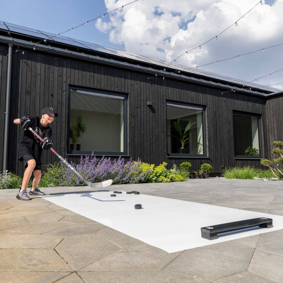 Young hockey player training with a rebounder and roll-up shooting pad on a backyard patio