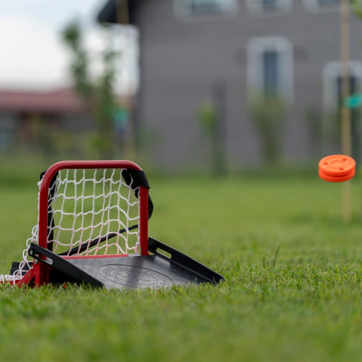 Hockey sauce catcher set up on backyard grass with orange puck flying toward the net