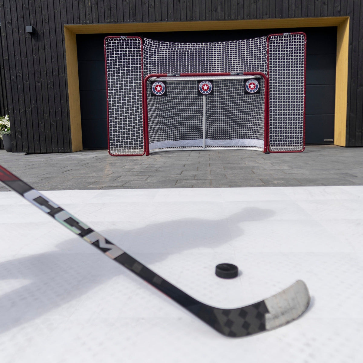 Hockey player on Better Hockey training tiles with a shooting setup including goal and targets in a driveway