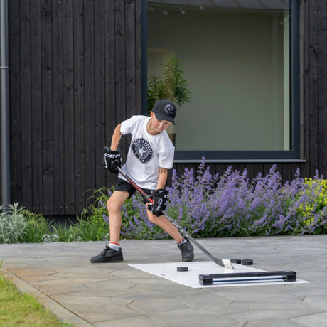 Young hockey player passing a puck into an Extreme Hockey Rebounder on a home patio