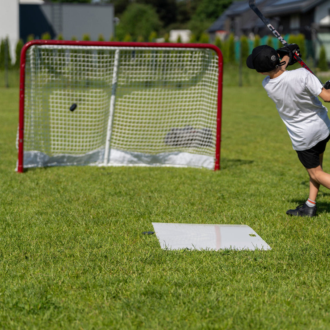 Young hockey player shooting a puck at a full-size goal in the backyard