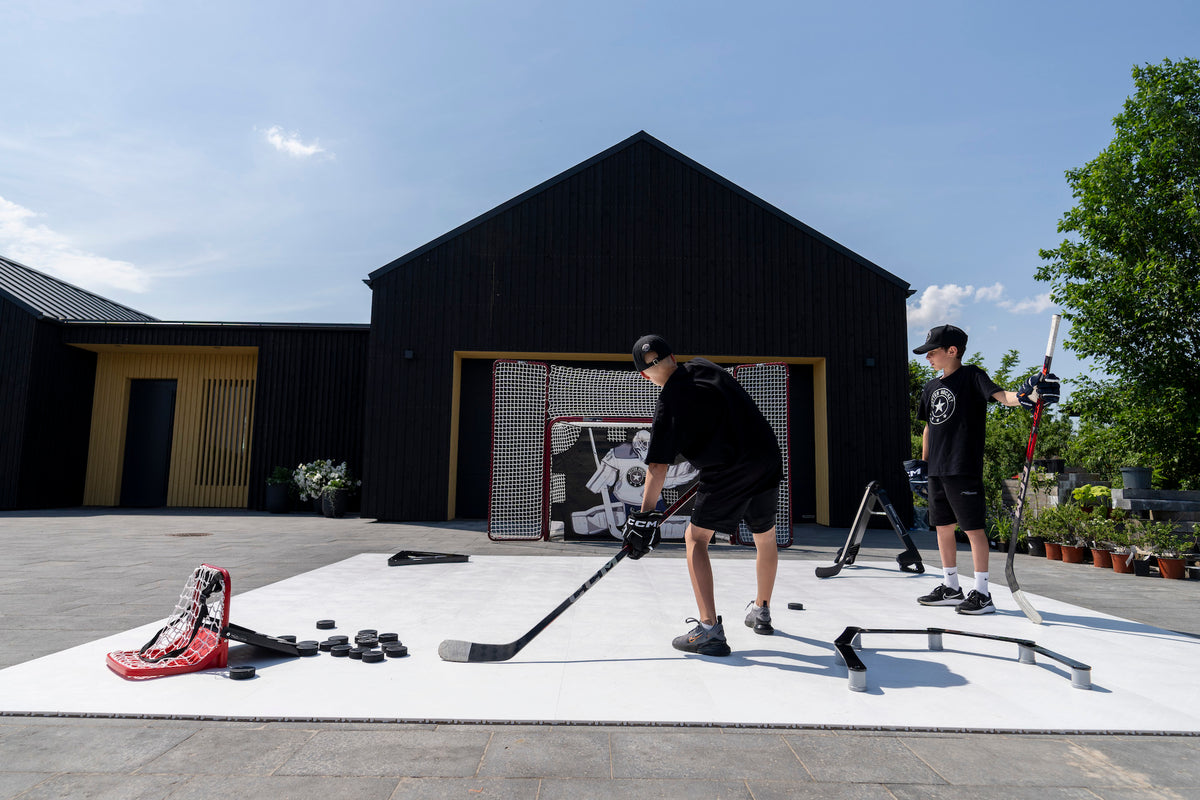 Två spelare tränar skott och passningar på plastis framför garaget