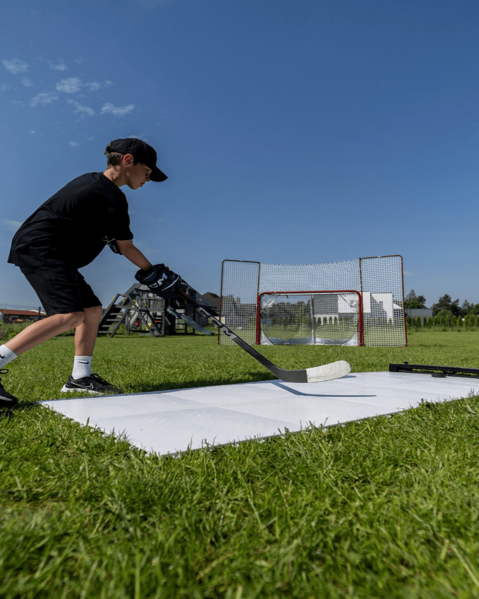Ung kille tränar hockeyskott på skottramp med målbur och hockeypassare i bakgrunden, perfekt för hockeyträning.