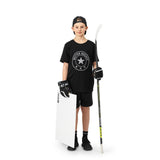 Ung hockeyspelare i svart t-shirt står med en hockeyklubba och en skottplatta, redo att träna sina färdigheter.